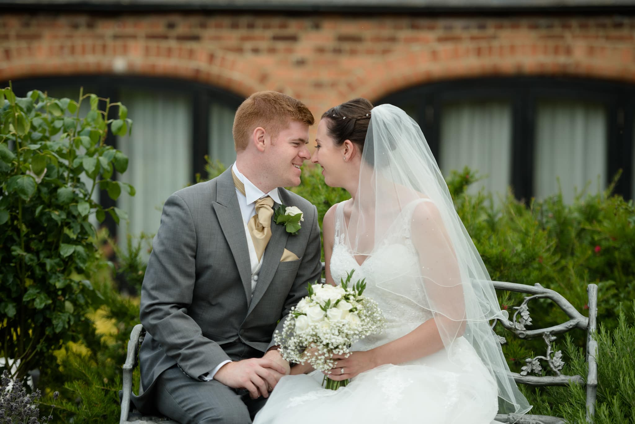 Bride and groom sitting on a bench with one of the barns in the background at Dodmoor House