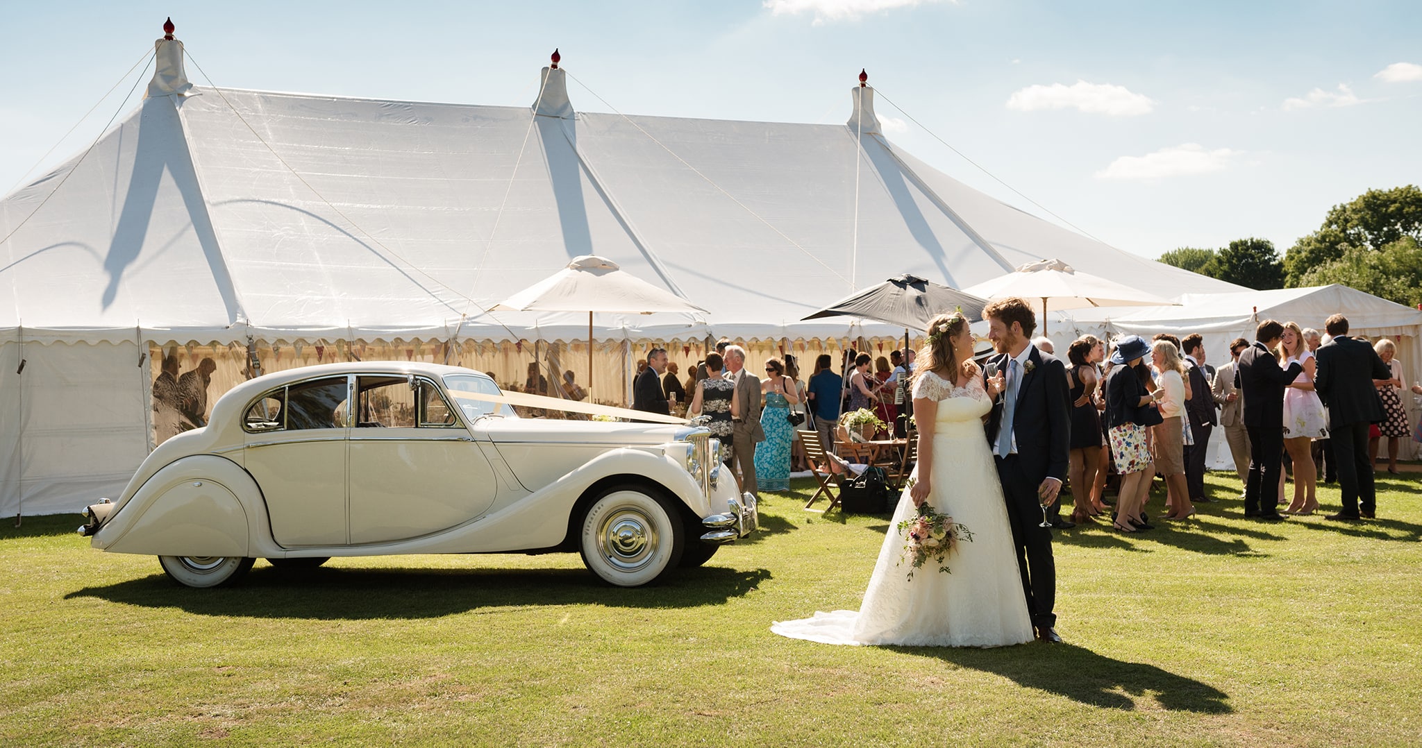 View of couple and wedding car against backdrop of relaxed marquee wedding