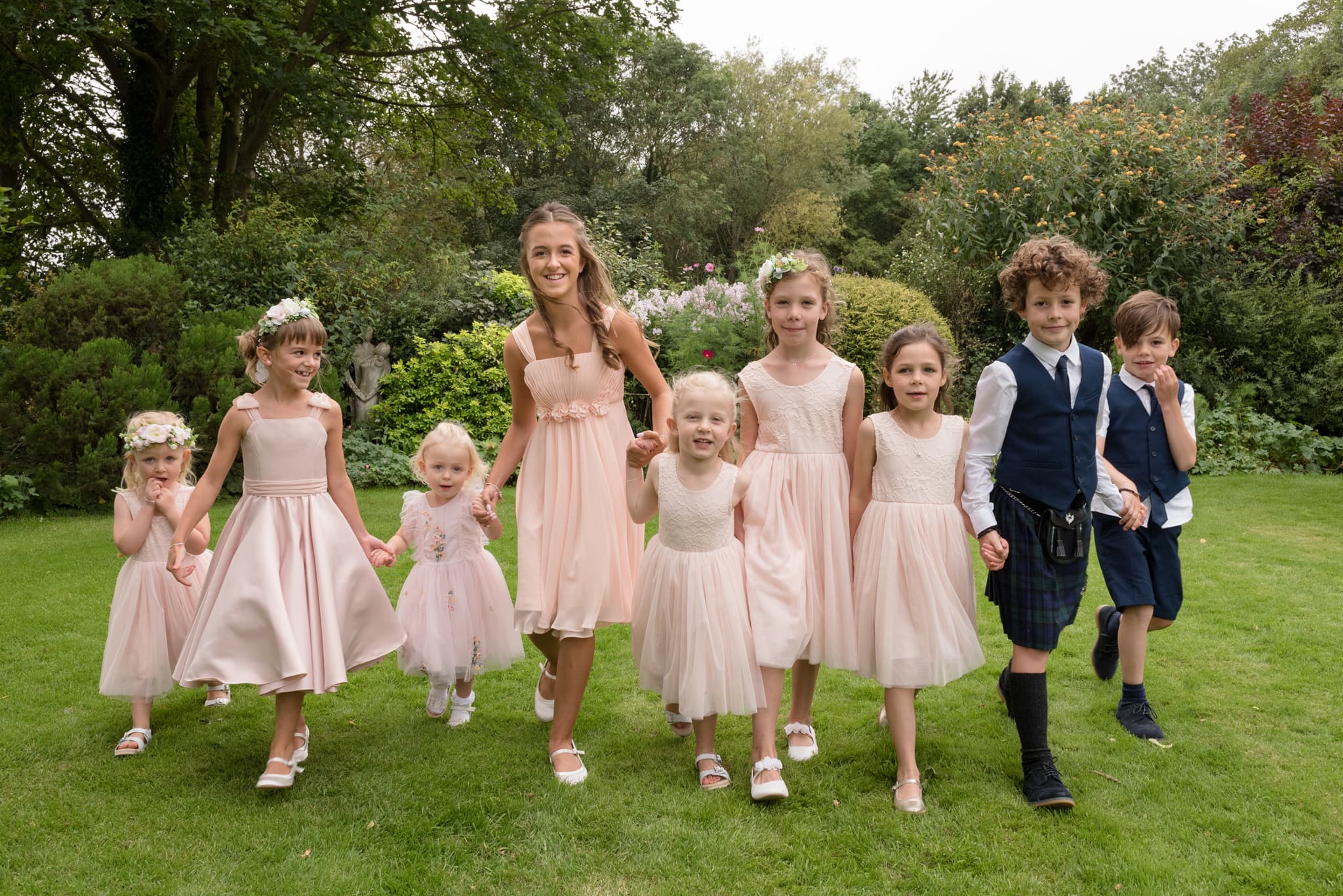 Flower girls and page boys walking hand in hand for a group photo