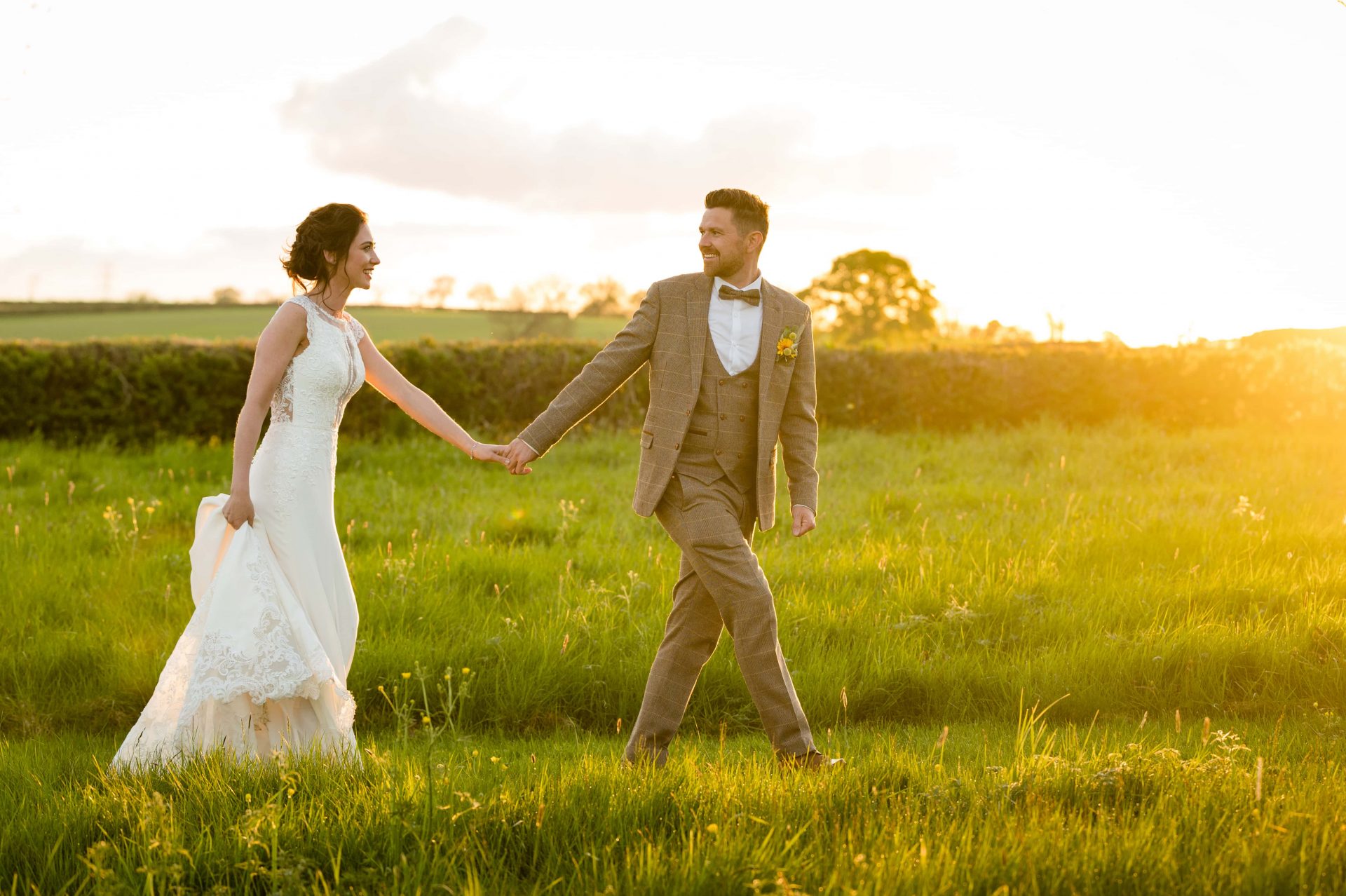 Bride and groom walking through field during golden hour at Hill Farm House in Brigstock