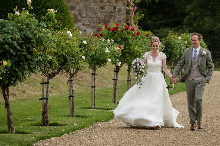 Bride and groom walking hand in hand through the rose garden at Rockingham Castle