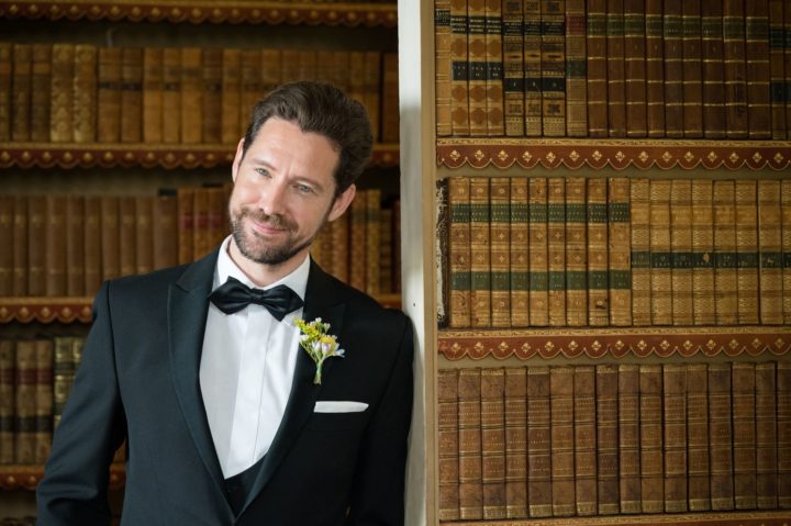 Close-up portrait of a groom standing beside a secret door in the bookcase