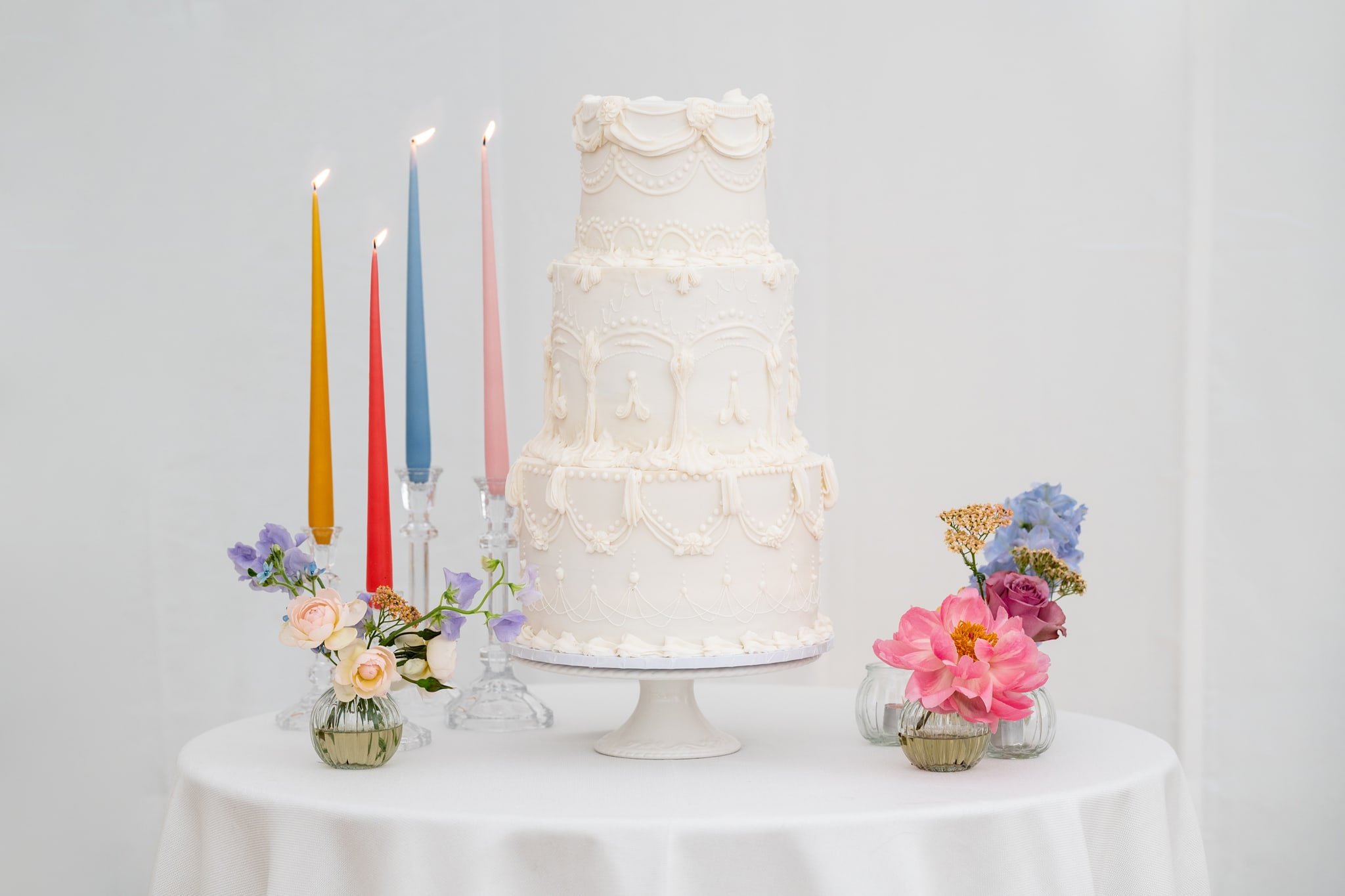 White iced wedding cake next to brightly coloured candles