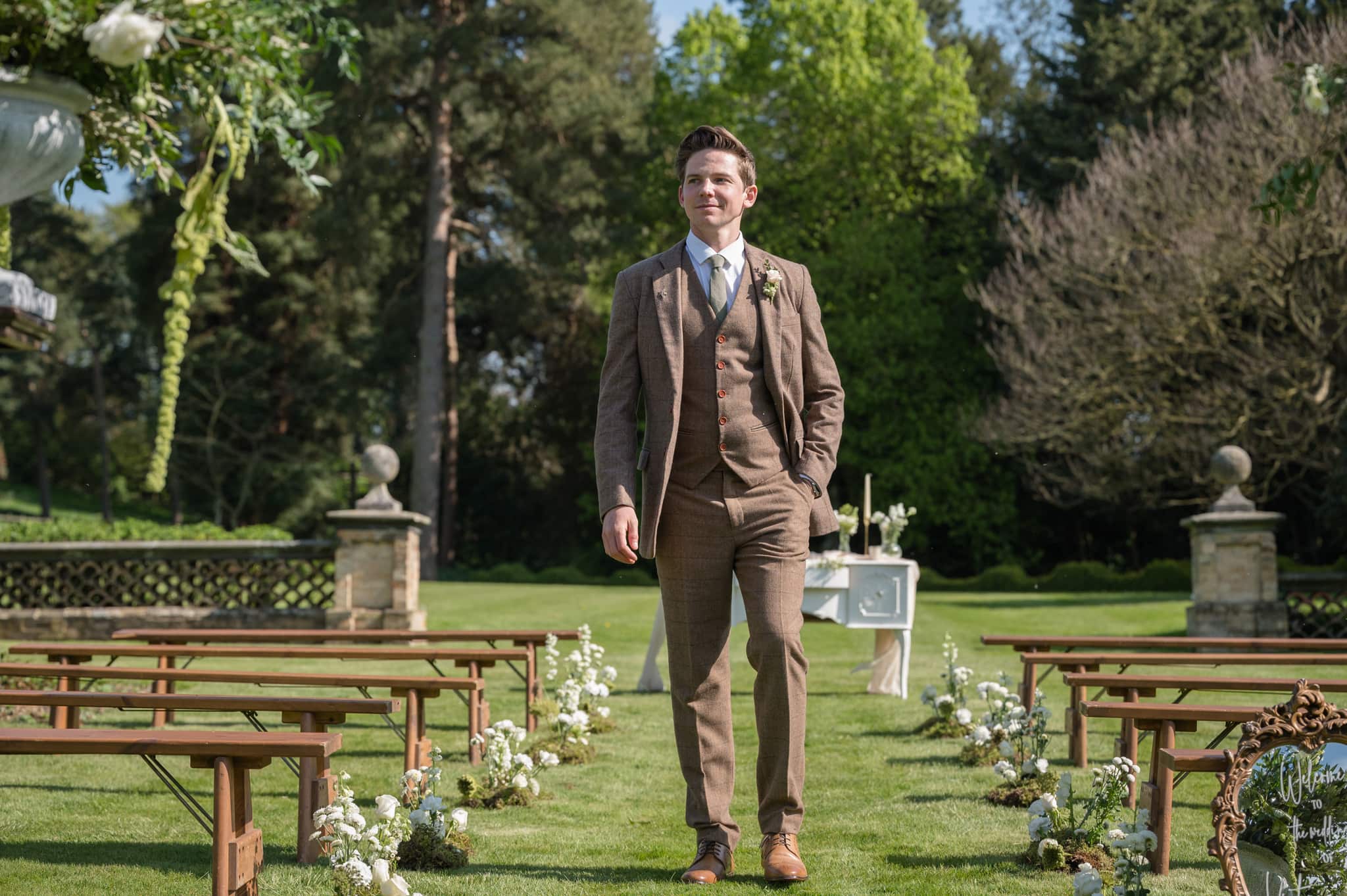 Groom standing between two rows of benches set-up for an outdoor wedding ceremony at Sutton Bonington Hall