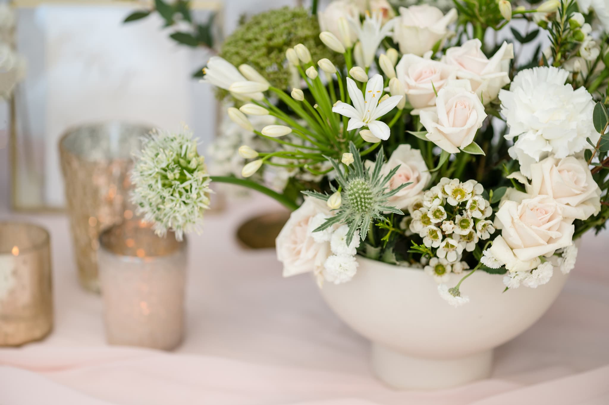 White spring flowers in a ceramic bowl on top of a pale pink table runner