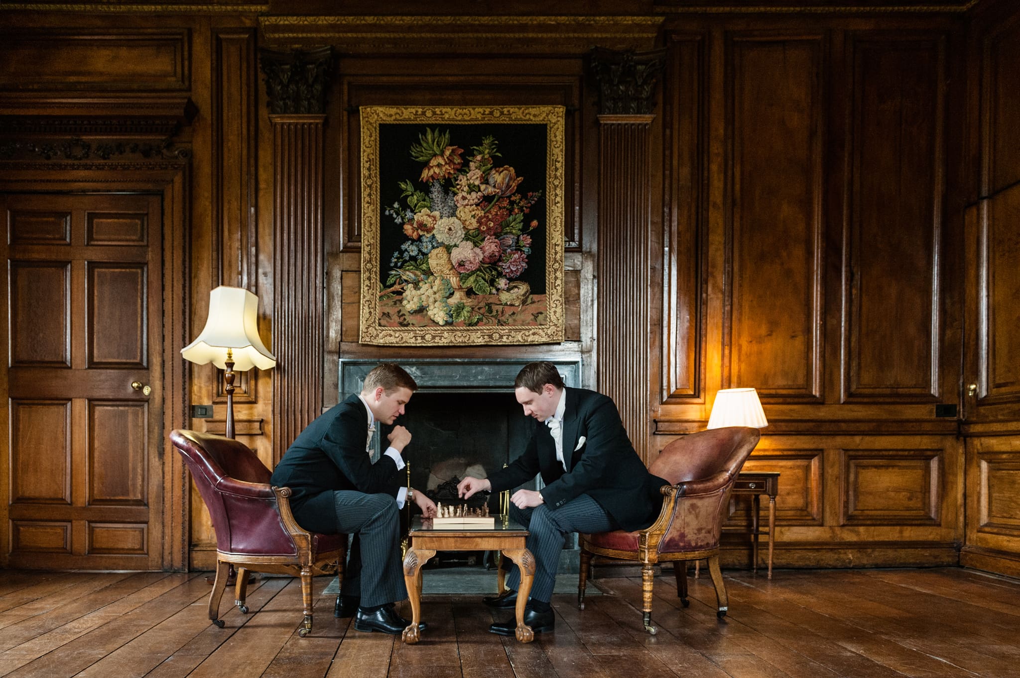 Groom and best man playing chess in front of a fireplace at Chicheley Hall