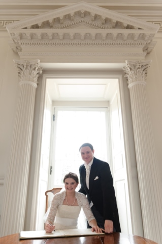 Posed photo of bride and groom framed in a doorway as they sign the marriage register