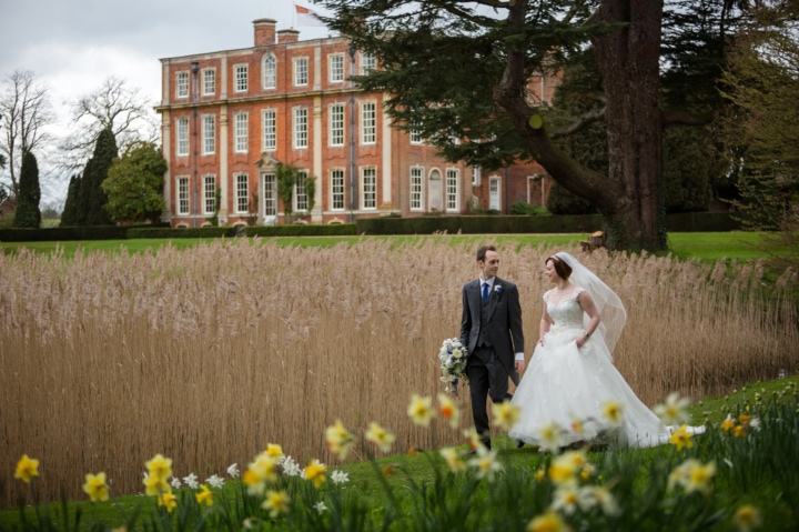 Bride and groom walking by the lake at Chicheley Hall with daffodils in the foreground