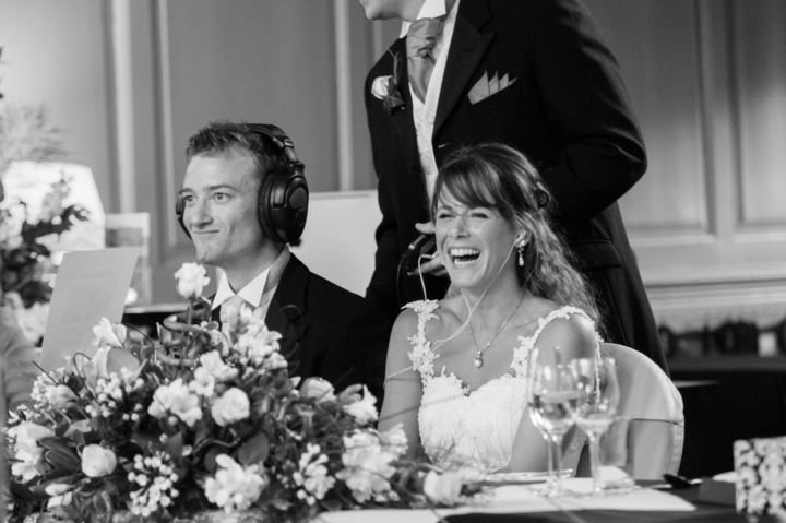 Groom wearing noise-cancelling headphones and pulling a face as he watches guests' reactions to his Best Man's speech