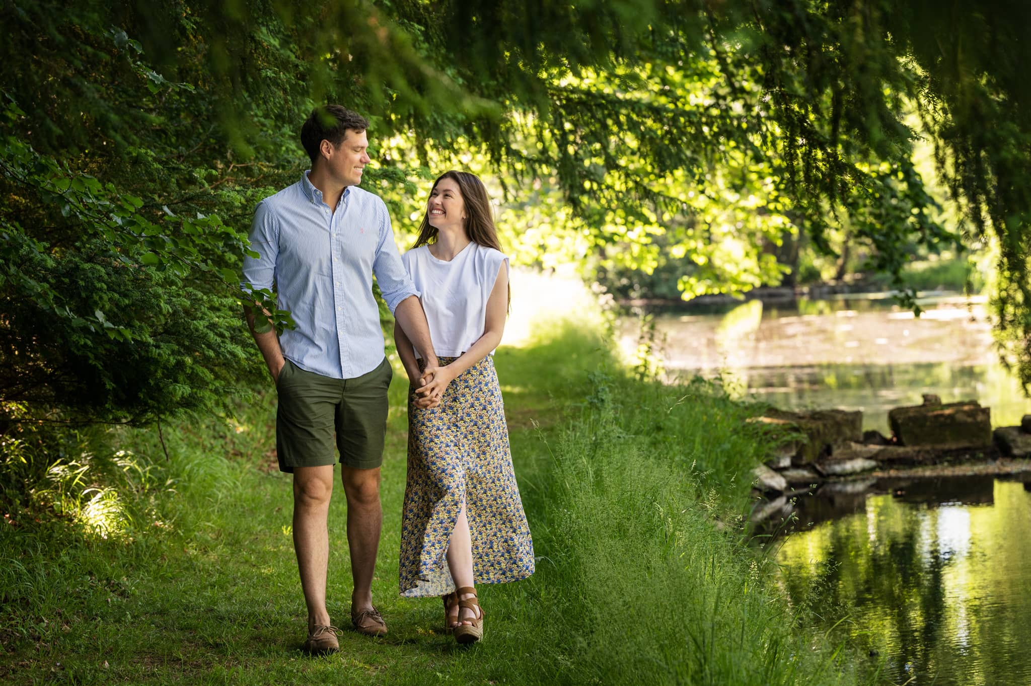 Engaged couple walking alongside a river through Exton Park estate