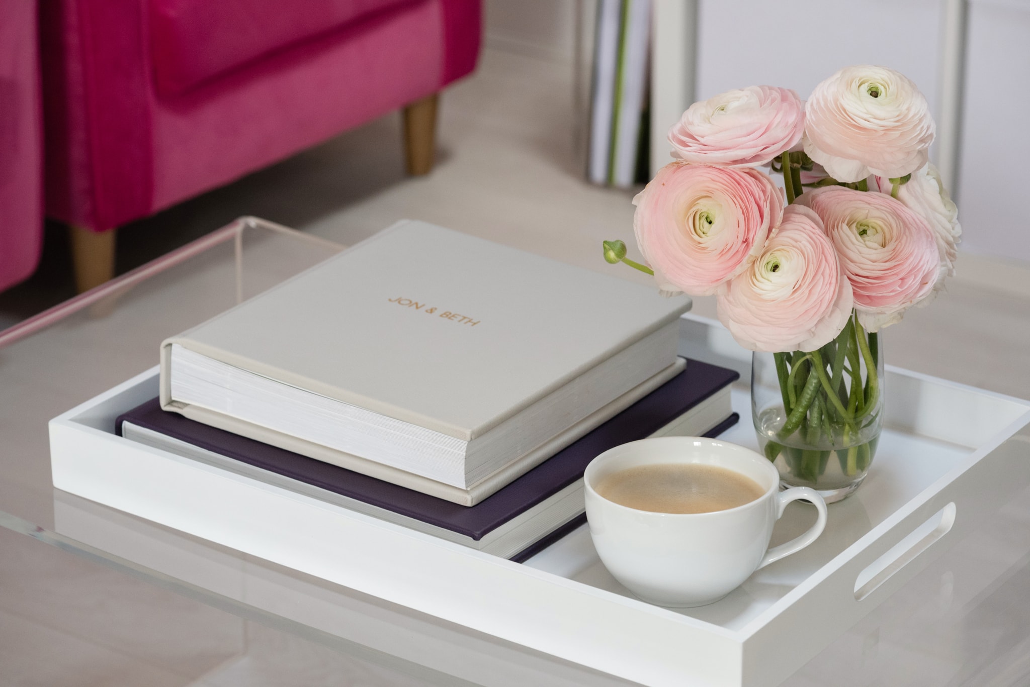 Two fine art wedding albums on a tray with a cup of coffee and pale pink ranunculus in a vase