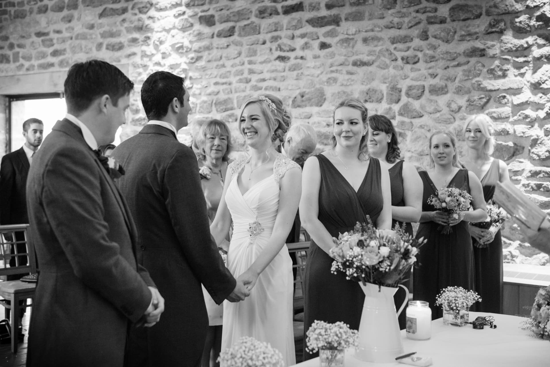 Bride grinning at the groom as they make their vows at Dodford Manor