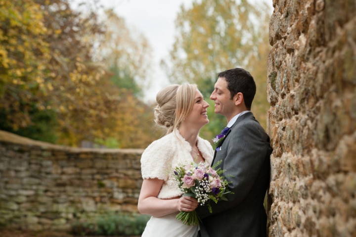 Bride and groom cuddled up by a stone wall at Dodford Manor