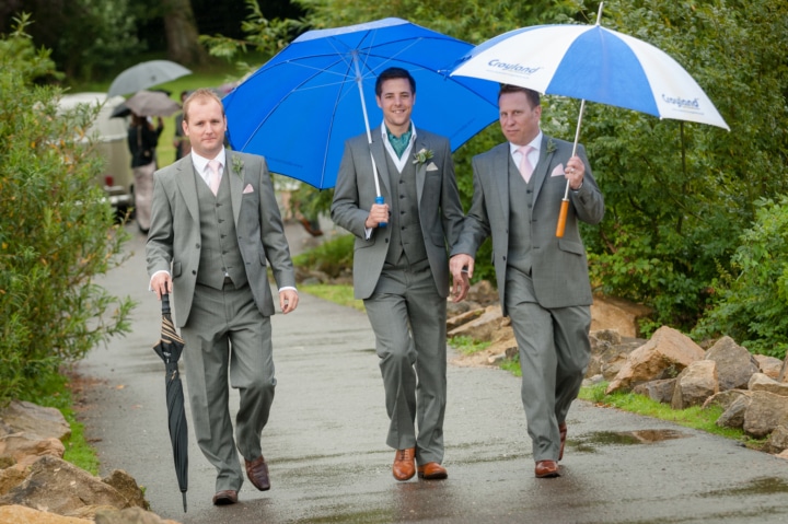 Groom and his best man holding umbrellas as they walk to Normanton church