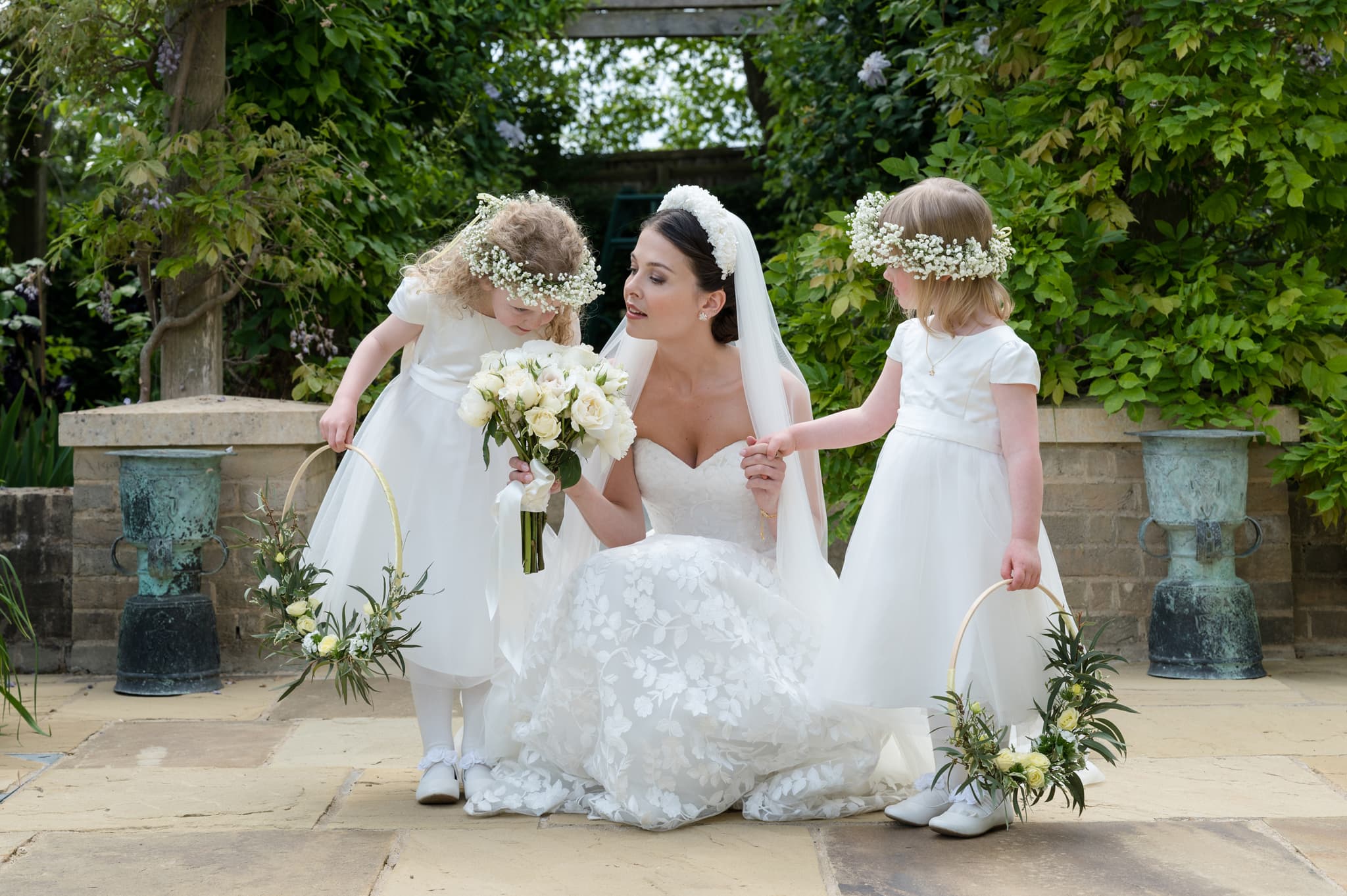Bride holding out her bouquet of white roses for her flower girl to smell