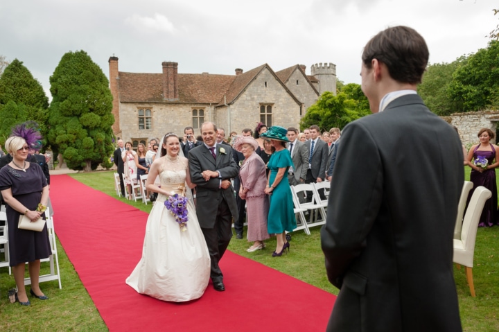 The bride walking down a red carpet aisle during an outdoor ceremony at Notley Abbey