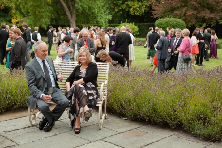 Two wedding guests chatting on a bench with all the other guests in the background at Notley Abbey