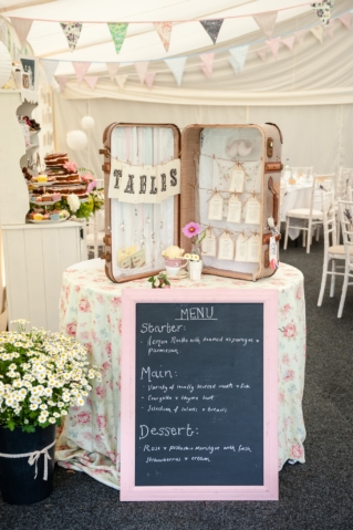 A suitcase table plan displayed on a floral linen covered table in a marquee