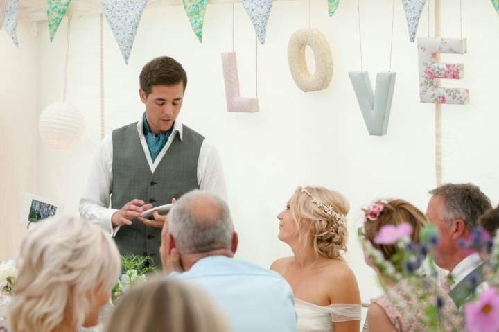 Groom speaking to the bride in his speech with LOVE letters hanging behind them