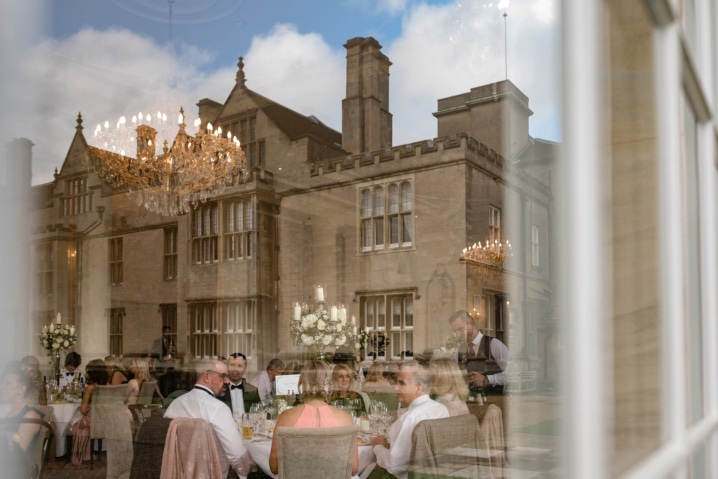 A picture through a window which shows both inside the room and a reflection of Rushton Hall in the glass