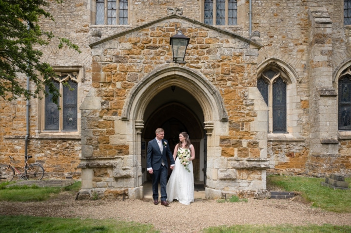 Bride and groom walking out of the door of Rushton church
