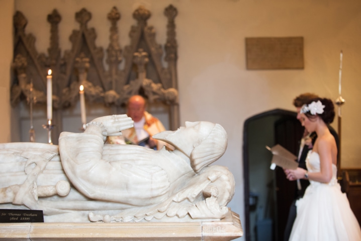 A marble tomb at Rushton church with a vicar, bride, and groom out of focus in the background