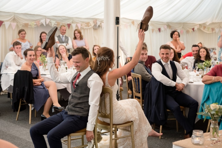 Bride and groom holding up their shoes in a game of Mr & Mrs in a marquee