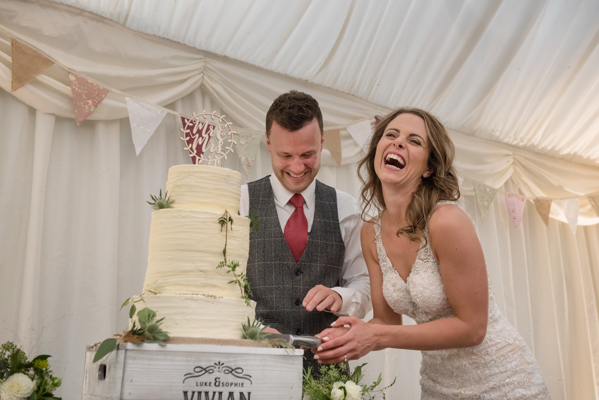 Bride laughing her head off as she and and groom cut cake
