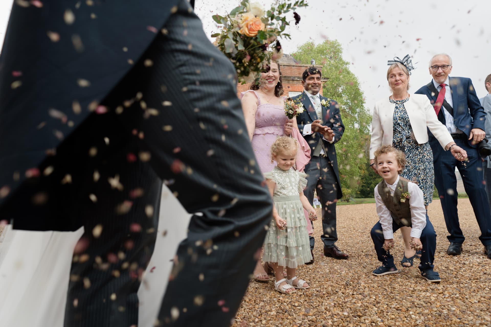 Page boy crouching ready to jump as he throws confetti at Kelmarsh Hall