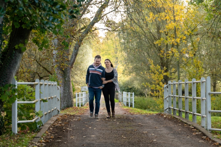 Engaged couple walking over a bridge with white railings