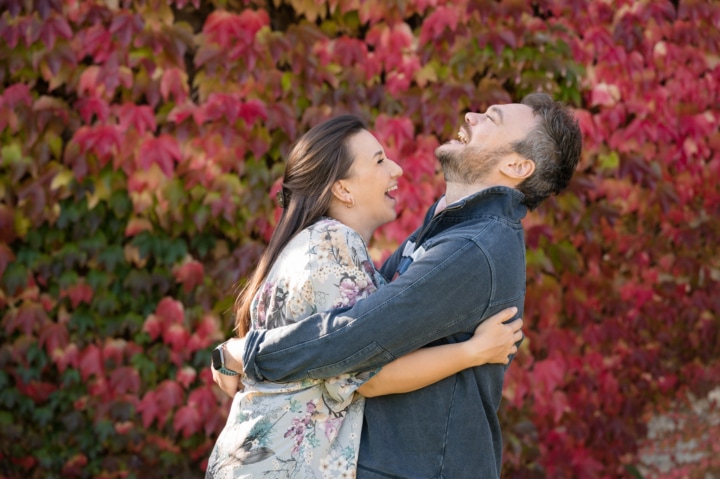Engaged couple laughing their heads off in front of an autumnal ivy clad wall