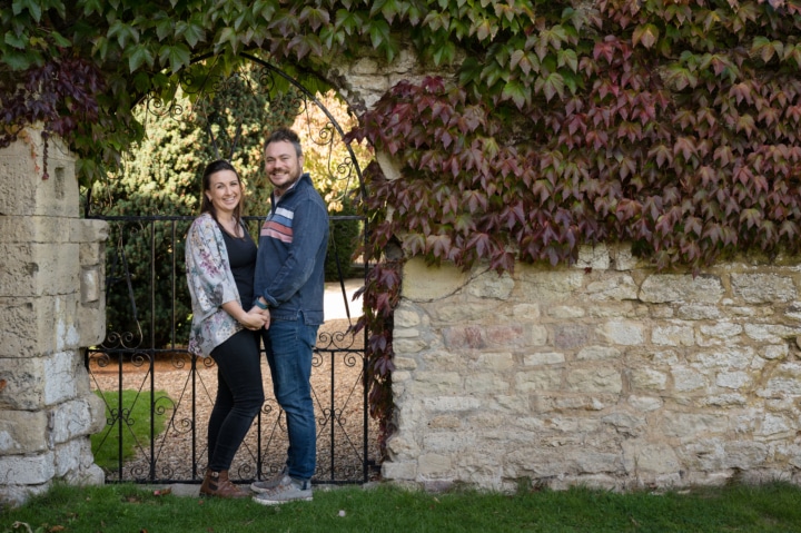 Engaged couple cuddled up in front of a wrought iron gate at Notley Abbey