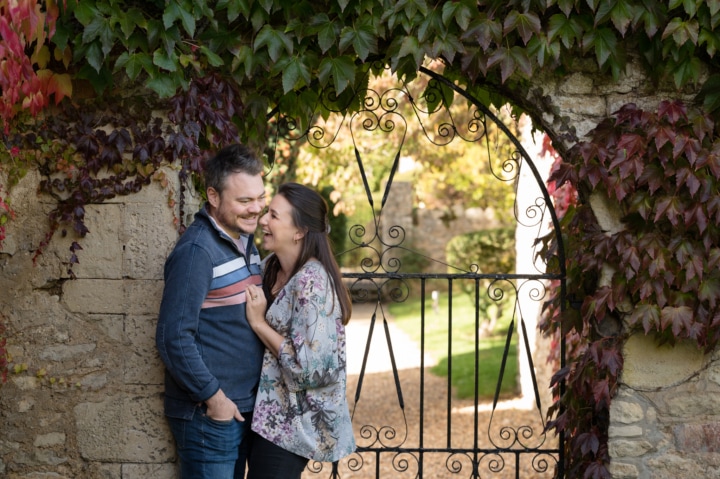 Engaged couple giggling in front of a decorative iron gate at Notley Abbey