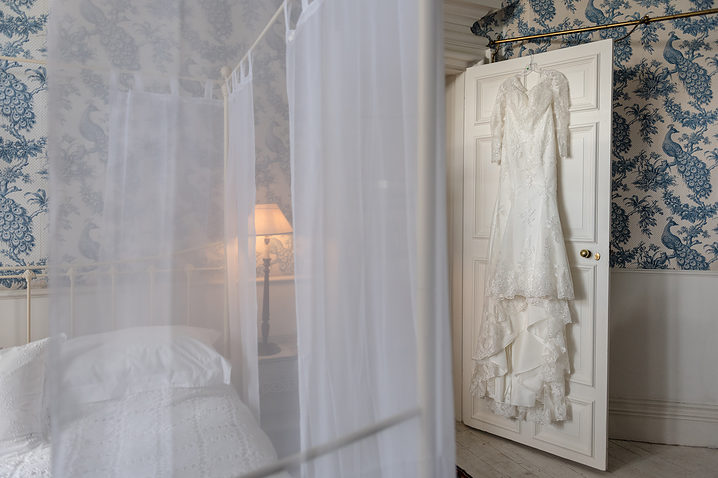 Wedding dress hanging on a white door with a four-poster bed next to it at Holdenby House