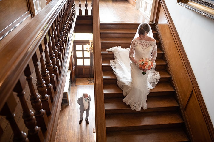 Bride walking down the stairs at Holdenby House as her Dad waits at the bottom for her