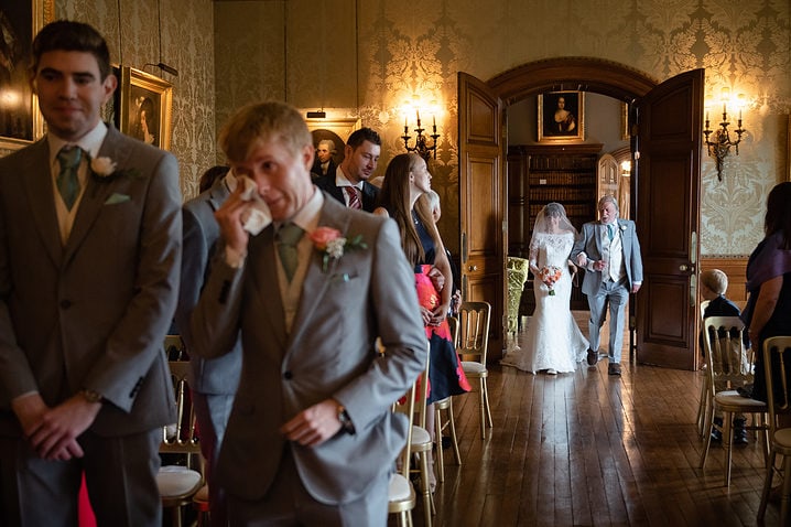Groom wiping away a tear as the bride walks down the aisle at Holdenby House
