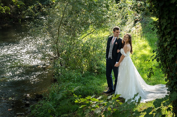Bride and groom standing by the river at Notley Abbey