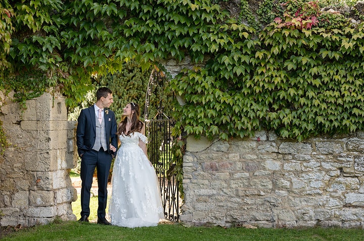 Bride and groom by a wrought iron gate and stone wall at Notley Abbey