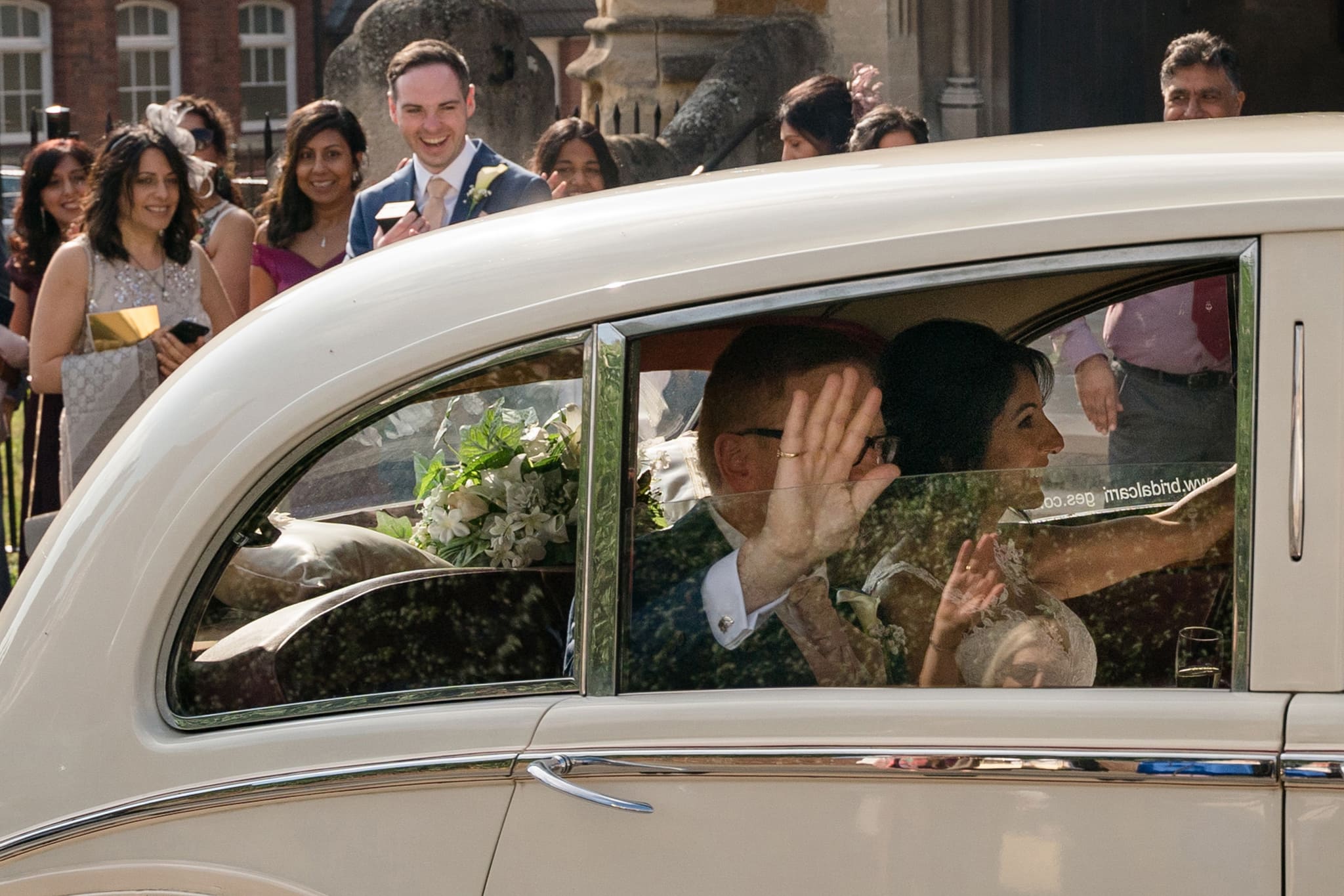 Groom waving out of the car window with his hand naturally obscuring his face