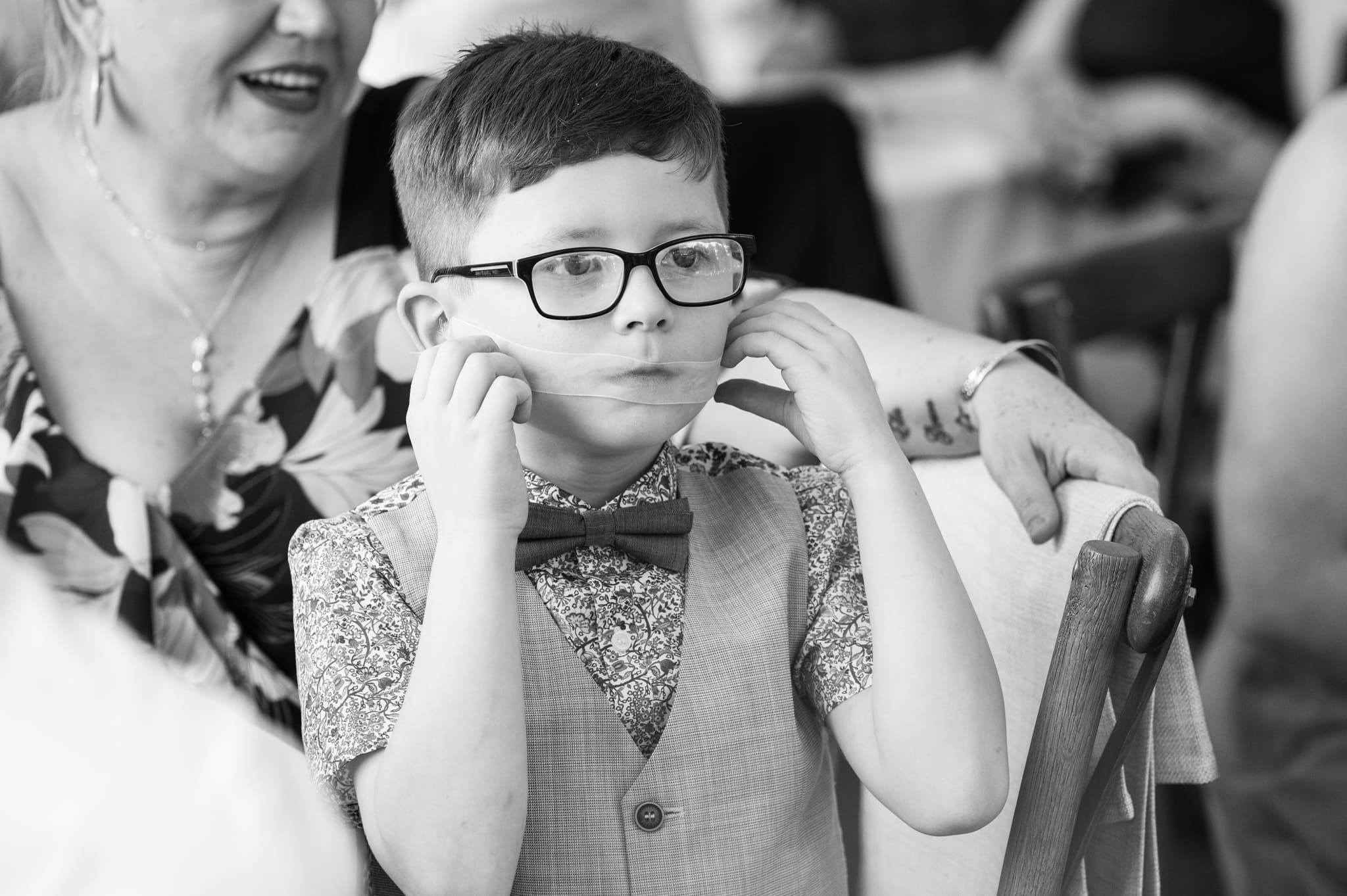Young wedding guest holding a piece of ribbon over his mouth