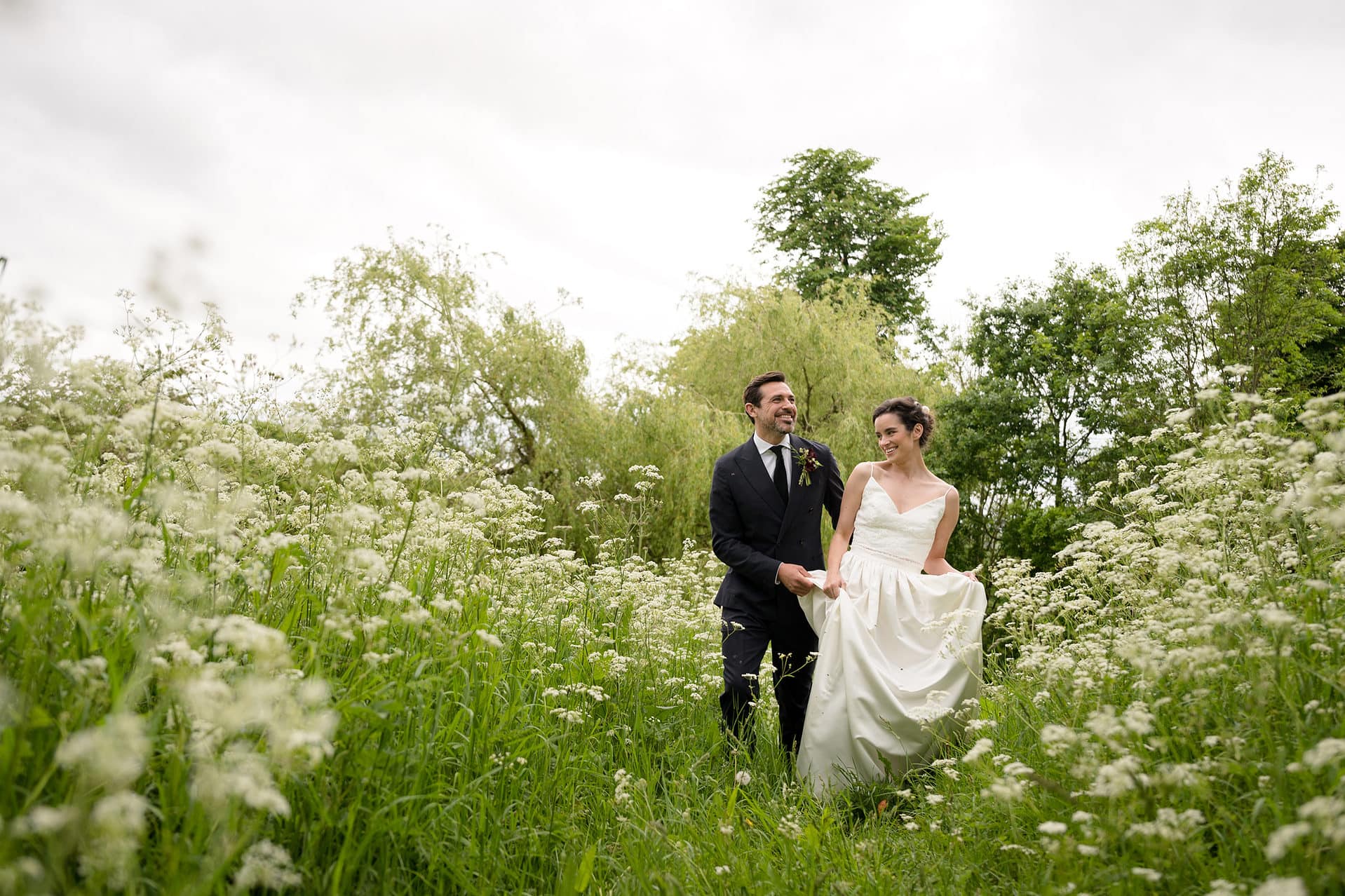 Bride and groom walking through a field of cow parsley
