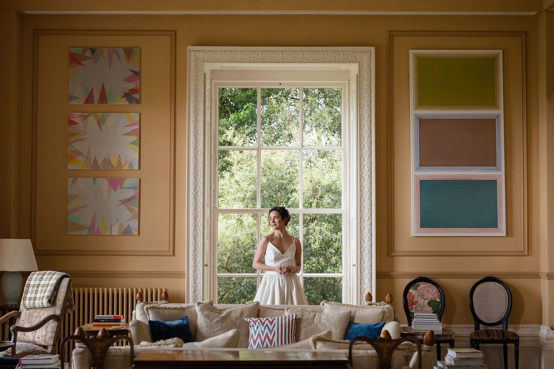 Bride standing in front of a tall window which has period moulding, framed either side with modern wall art