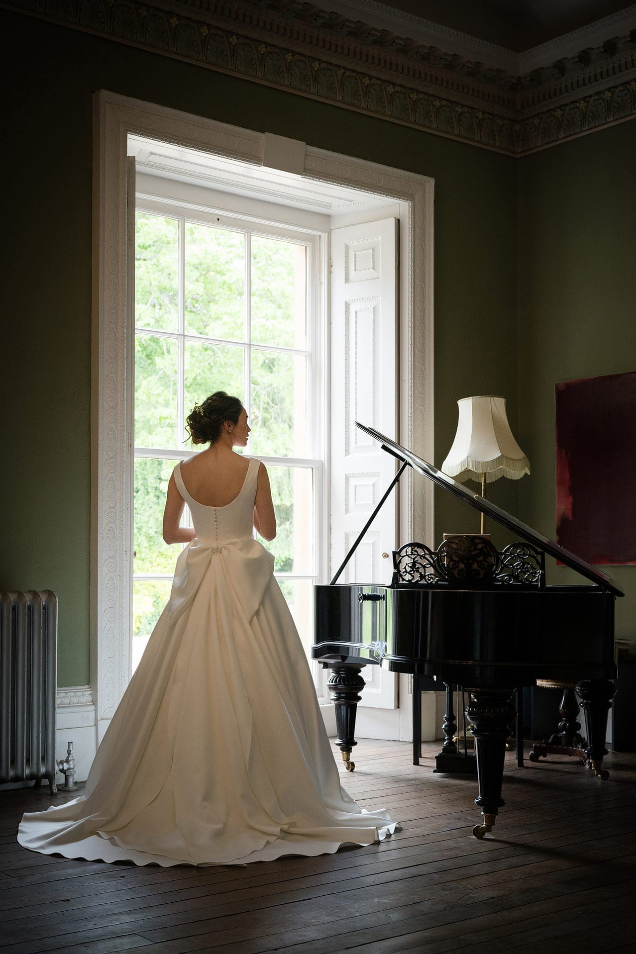 Bride standing next to a grand piano in front of a floor-to-ceiling window