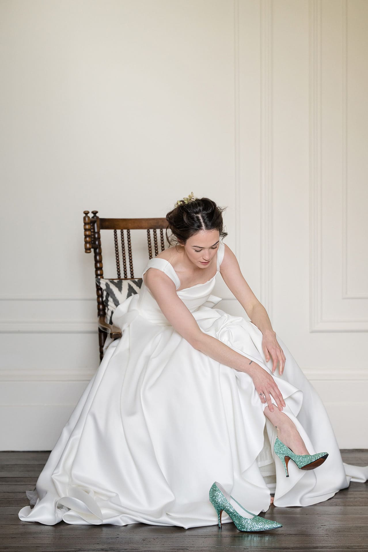 Bride sitting on an antique rocking chair to put on a pair of green sparkly Victoria Beckham shoes