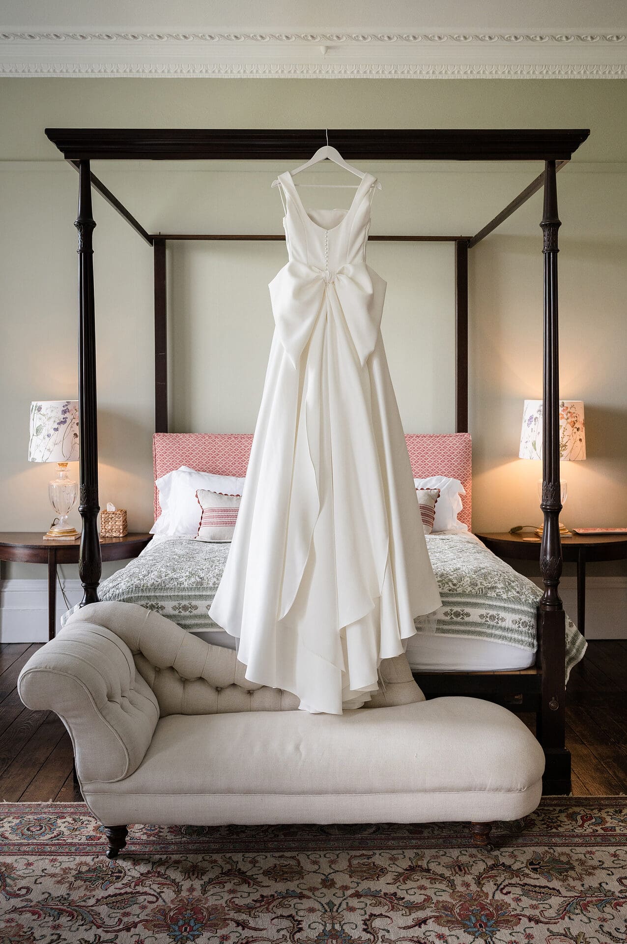 A wedding dress hanging on the end of an antique four-poster bed