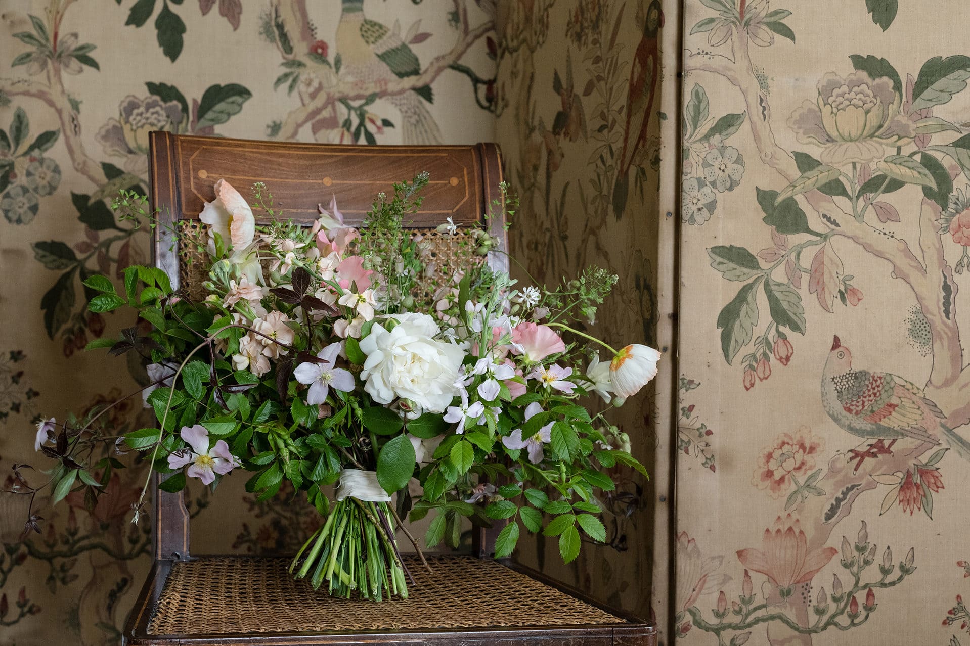 A wild but pretty hand-tied wedding bouquet on an antique chair in front of a chinoisserie-style concertina screen