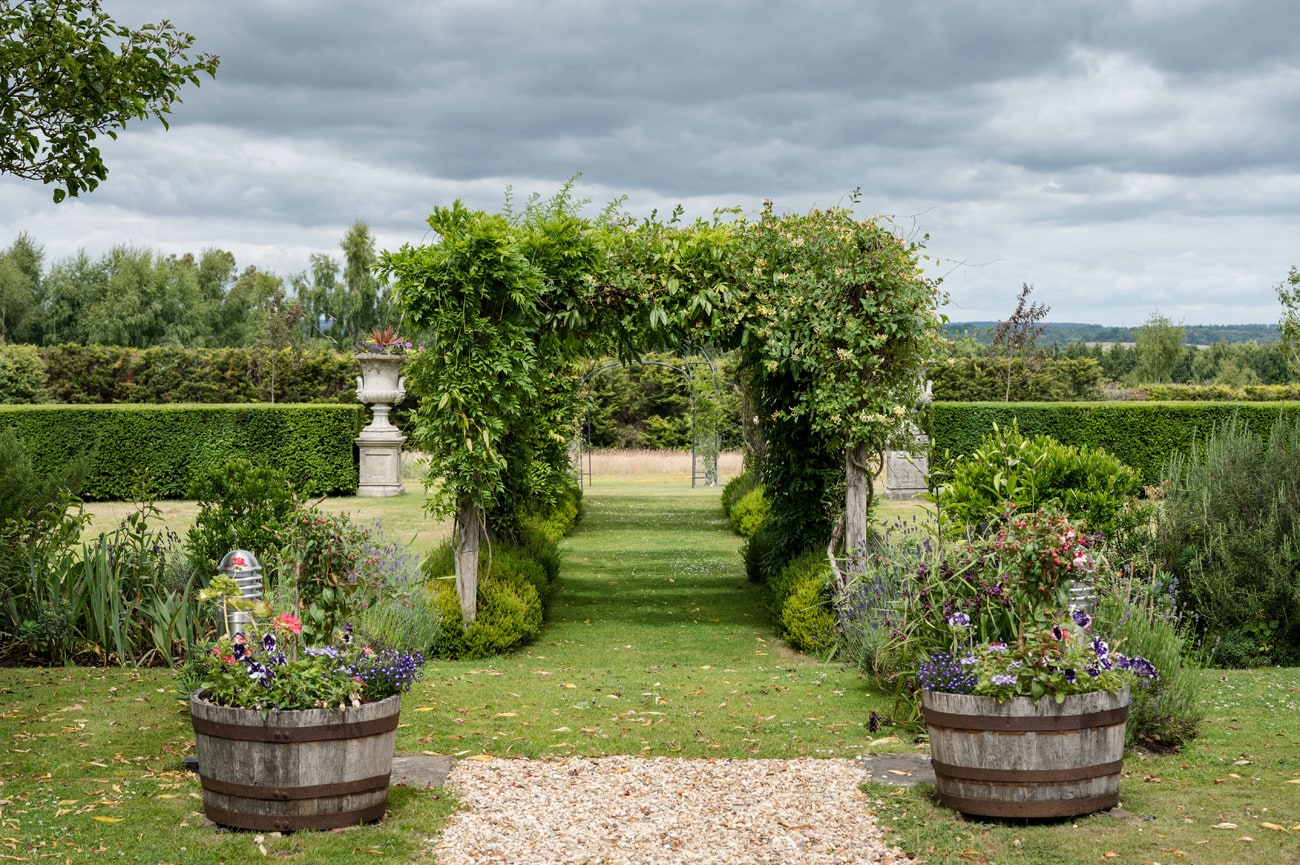 The landscaped gardens at Cain Manor with a pergola and wooden barrels planted with colourful summer flowers