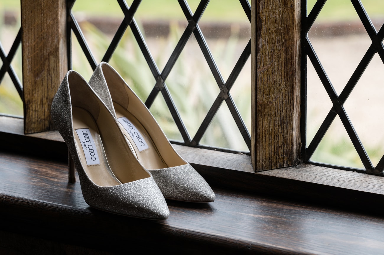 A pair of sparkly Jimmy Choo wedding shoes on a window sill with a section of the leaded window behind