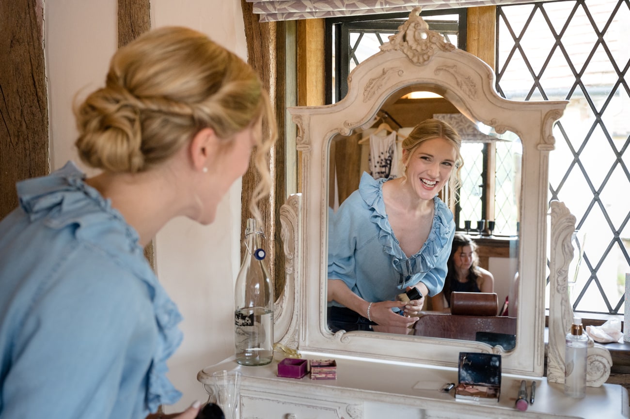 Bride smiling in a mirror as she laughs with one of her bridesmaids