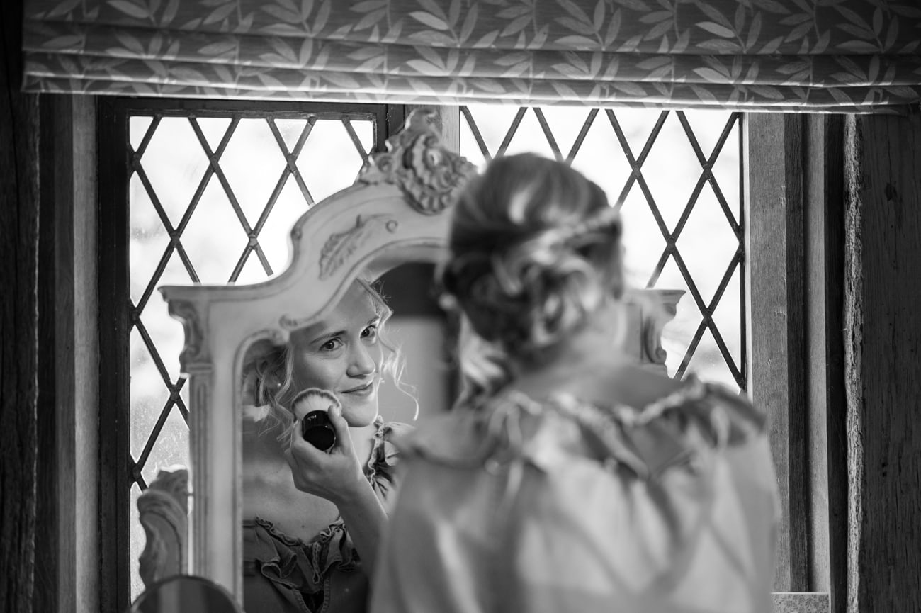 Bride putting blusher on in an ornate white mirror